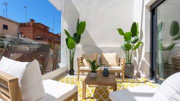 Een balkon met een bank, stoelen, een tafel en planten in potten.