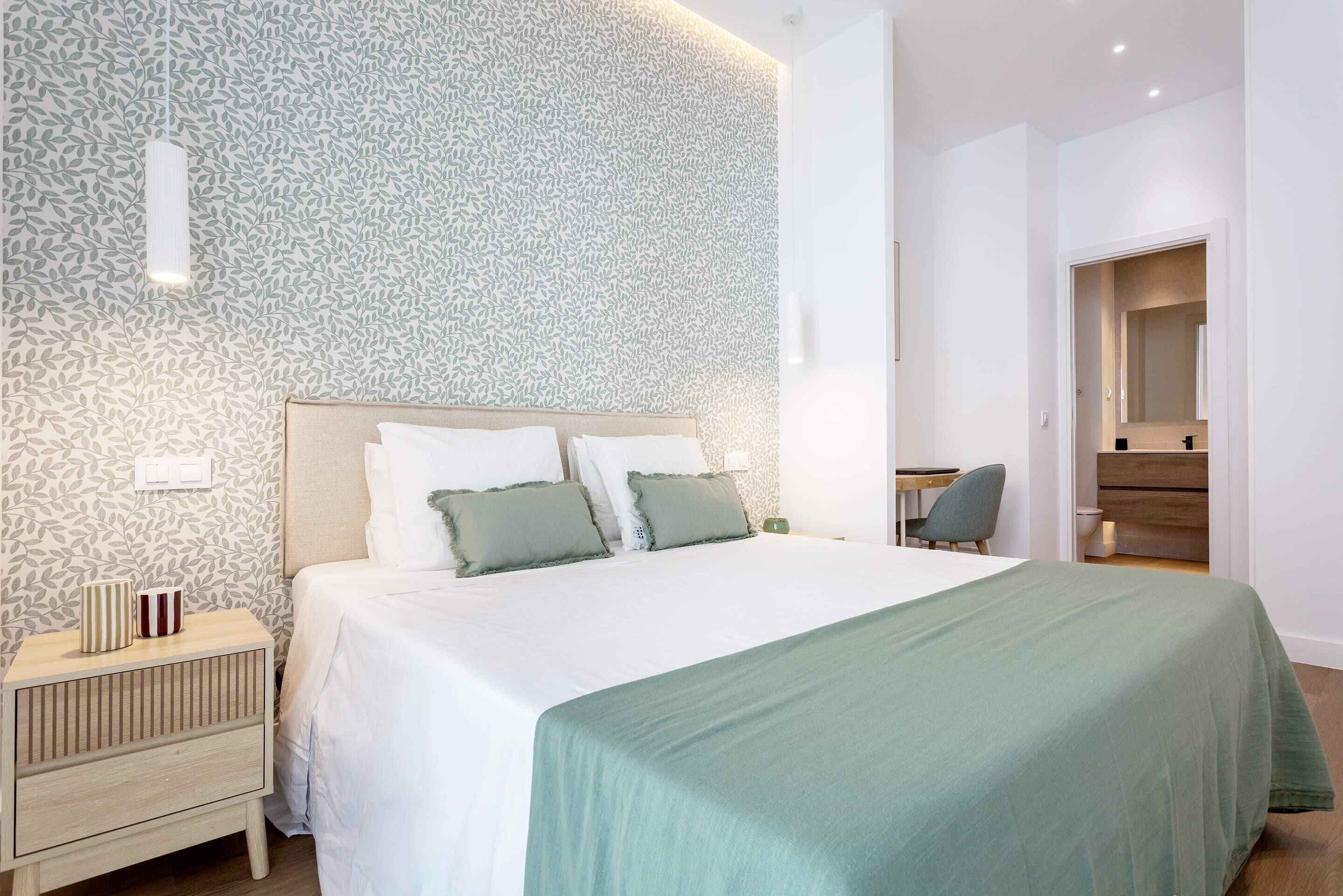 Een moderne slaapkamer met een groot bed, een nachtkastje, een stoel en een bureau.