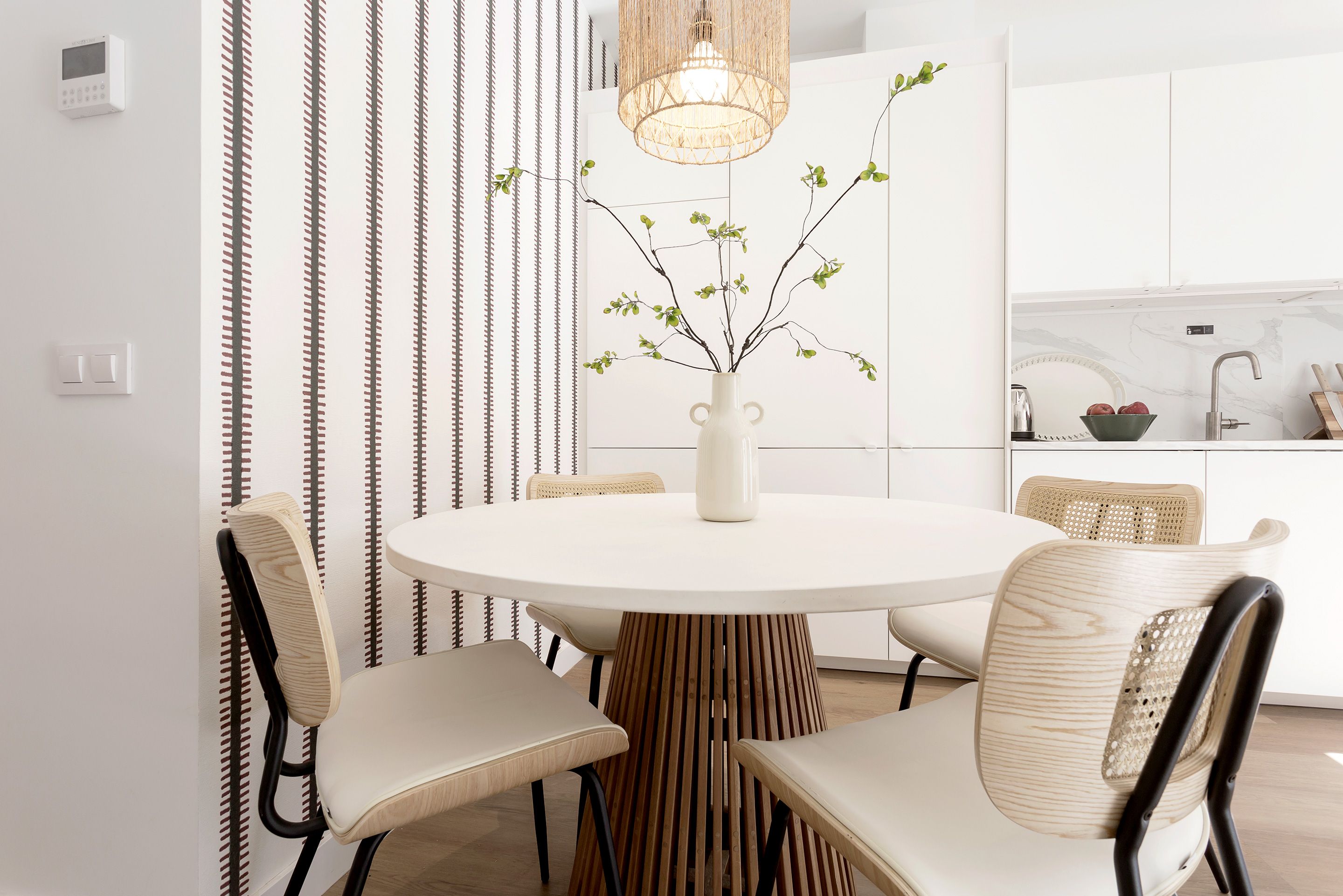 A modern dining area with a round table, white chairs, a vase with branches, and a hanging light fixture.