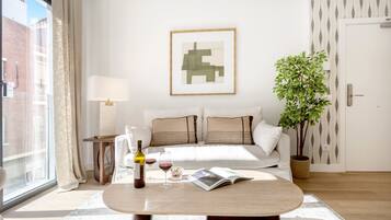 Una sala de estar moderna con sofá, mesa de centro, lámpara, cuadro enmarcado, planta en maceta y ventana con cortinas.