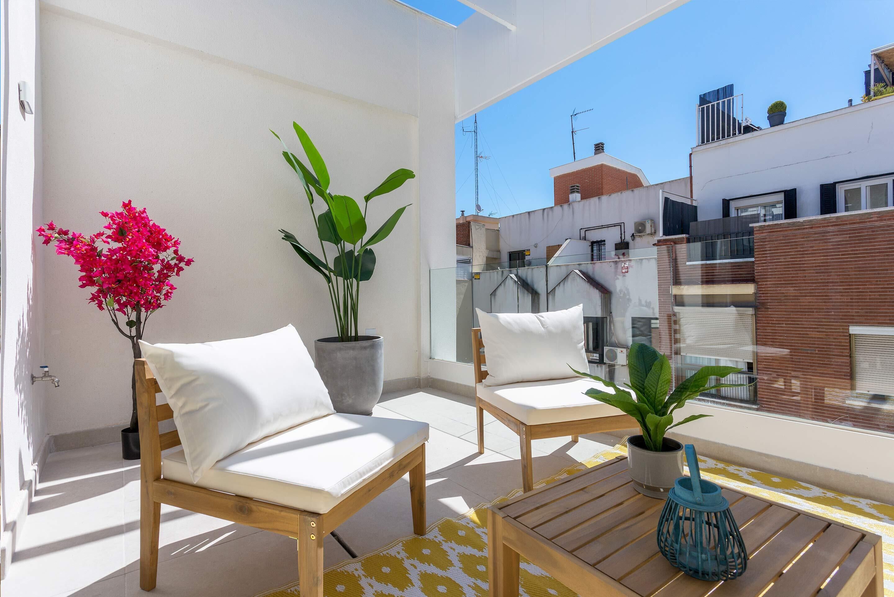 Een balkon met twee houten stoelen, een kleine tafel, een bloempot en een bloemstuk.