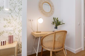 Ein Zimmer mit Schreibtisch, Stuhl, Spiegel, Lampe und einer Topfpflanze.