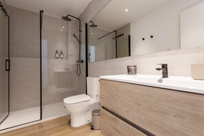 A modern bathroom with a glass-enclosed shower, a toilet, and a vanity with a mirror. - Genteel Home Zabaleta (Madrid)