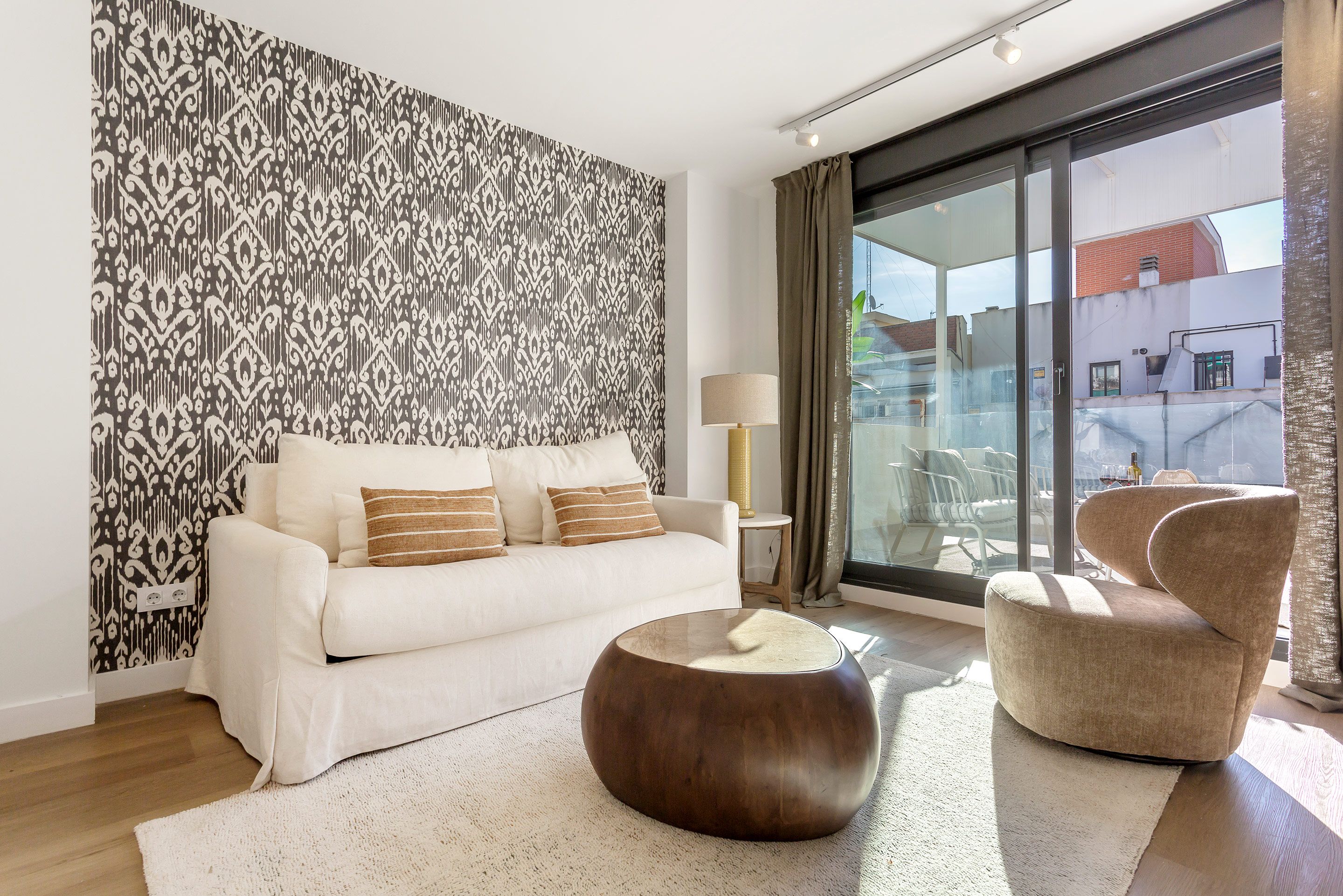 Una sala de estar moderna con un sofá blanco, una mesa de centro redonda de madera y una pared con estampado.