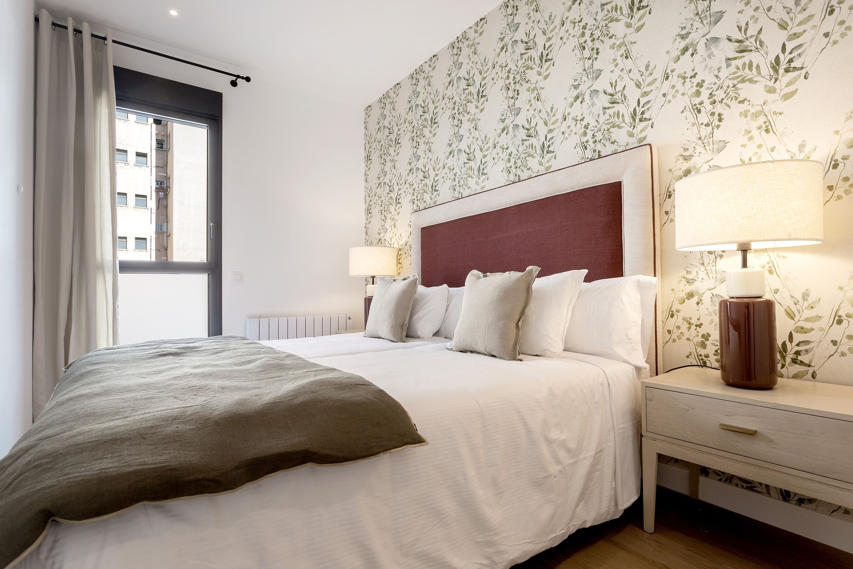 Una habitación de hotel con cama, mesitas de noche, lámpara y ventana con cortinas.