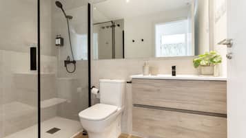 Un baño moderno con ducha de vidrio, inodoro, tocador con espejo y una planta en maceta.
