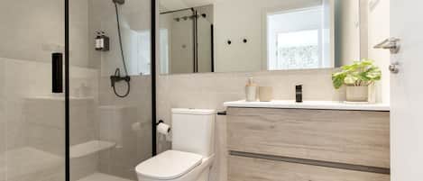 A modern bathroom with a glass-enclosed shower, a toilet, a vanity with a mirror, and a potted plant.
