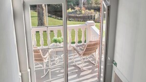 Een glazen deur die leidt naar een balkon met rieten stoelen en een kleine tafel.