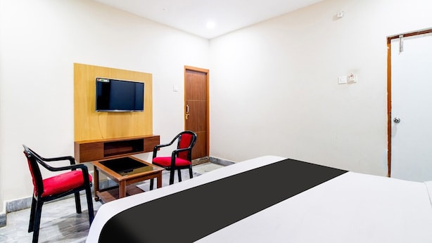 A hotel room with a bed, a TV mounted on the wall, a wooden desk, two chairs, and a wardrobe. - Super Hotel O Gurudwara (Visakhapatnam)