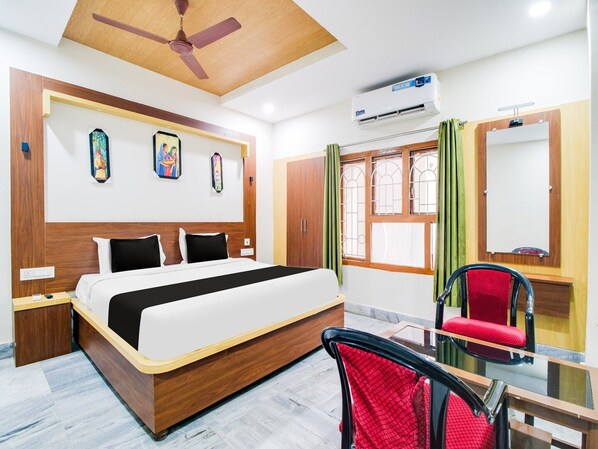 A hotel room with a bed, a chair, an air conditioner, a mirror, and a window with curtains.