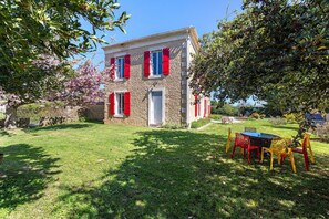 A stone building with red shutters, a lawn, and a table with chairs.