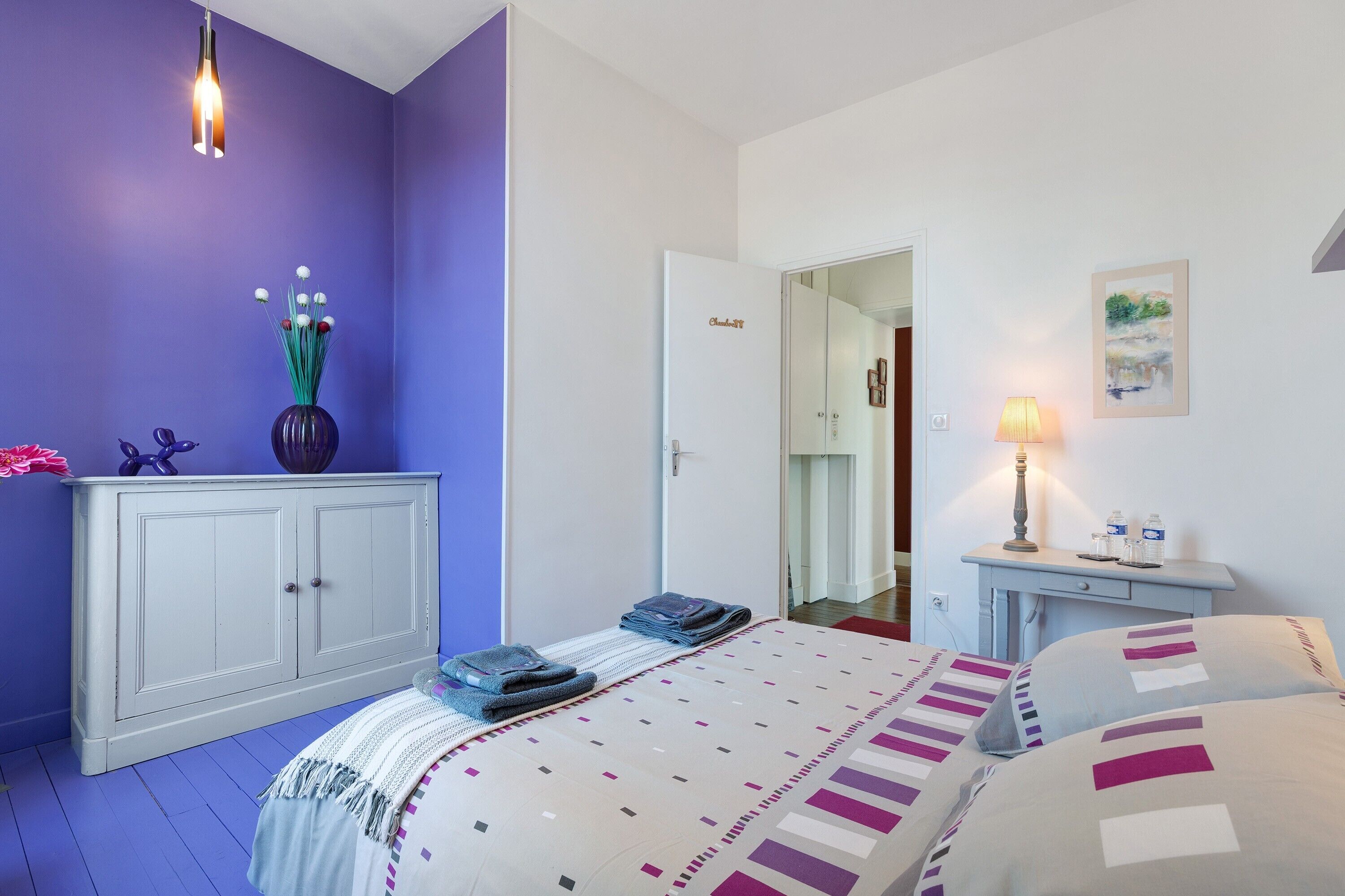 Ein Schlafzimmer mit einem Bett, einem Nachttisch, einer Kommode, einem Spiegel und einer Tür zu einem anderen Raum.