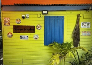 A yellow building with a blue door, various stickers, and a sign that reads 'WELCOME'. - Charming accommodation in Gosier, 5 minutes from the beaches (Le Gosier)