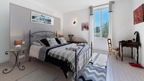 Ein Schlafzimmer mit Bett, Nachttisch, Lampe, Sessel und Schreibtisch mit Computer.