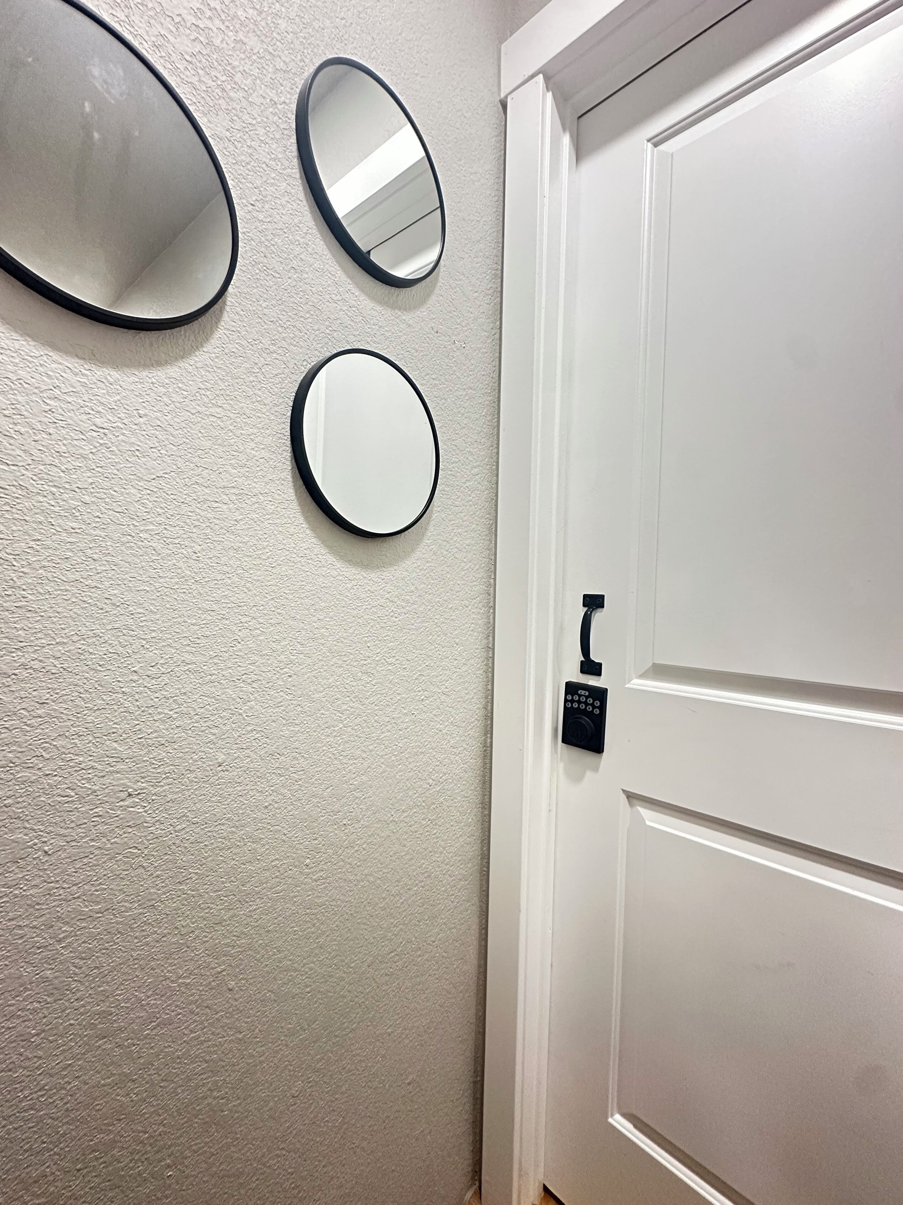 A white door with a keyhole and a small black sign, three round mirrors on the wall, and a textured wall.