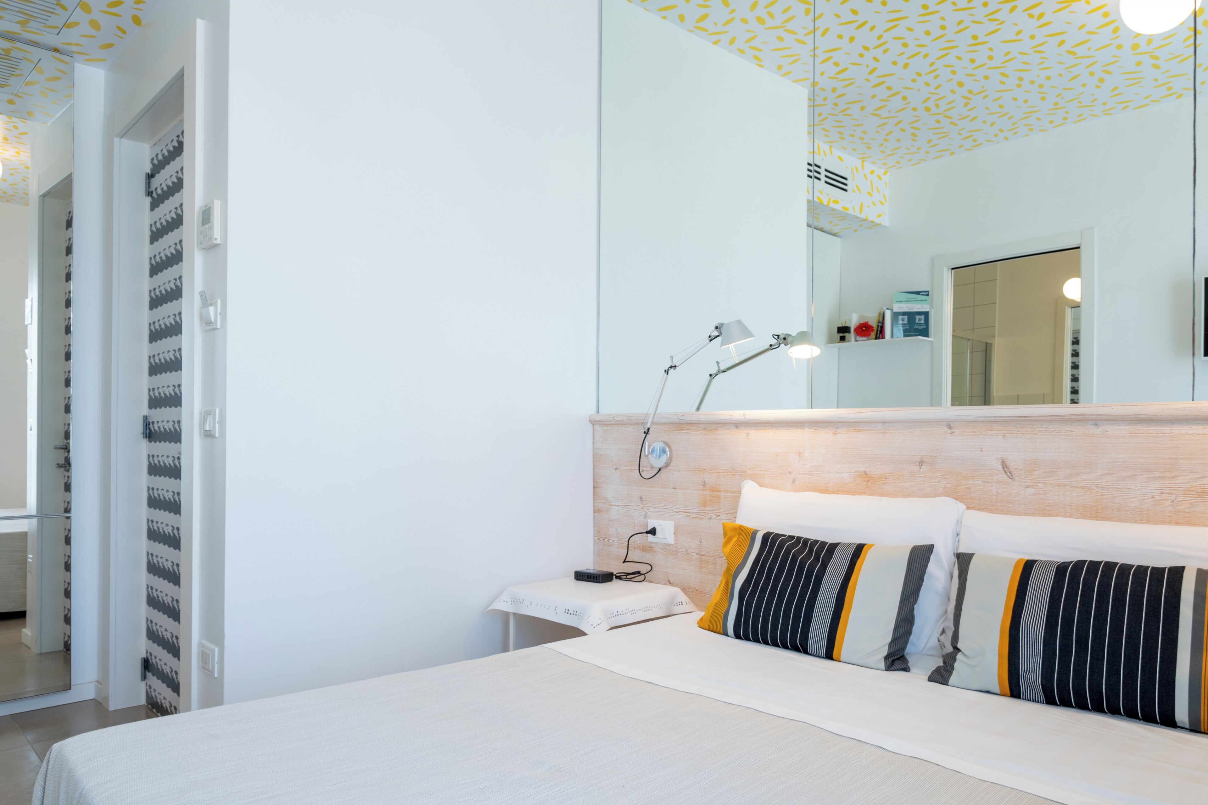 Un dormitorio con cama, mesita de noche, lámpara y espejo en la pared.