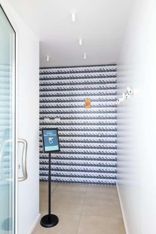 A hallway with patterned wallpaper, a sign indicating a holiday room collection, and a small decorative item on the wall. - Hotiday Porto Cesareo Laguna (Porto Cesareo)