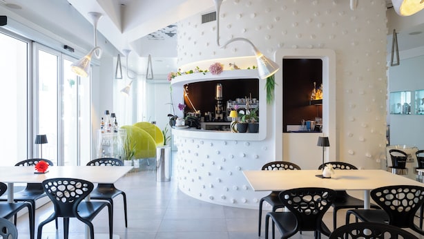 A modern interior with a curved reception desk, black chairs, and a white ceiling with a unique pattern. - Hotiday Porto Cesareo Laguna (Porto Cesareo)