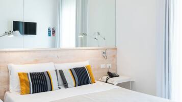A modern hotel room with a large bed, a wooden headboard, a bedside table, a nightstand, a mirror, and a ceiling with a leaf pattern.