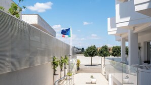A modern building with a glass railing, a flag, and potted plants. - Hotiday Porto Cesareo Laguna (Porto Cesareo)
