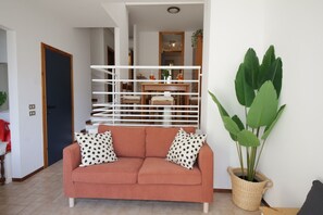 A living room with a sofa, two patterned pillows, a large green plant, and a white railing. - La Dolce Vita - Lake Como - Tremezzo - near the lake (Tremezzo)