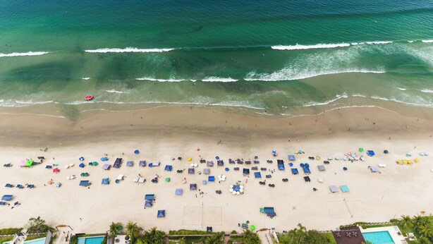 Vista aérea de una playa con zona de piscina, sombrillas y cancha de voleibol.