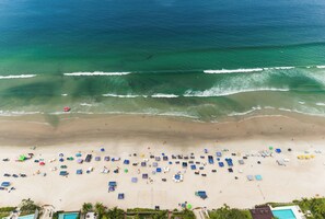 An aerial view of a beach with a pool area, beach umbrellas, and a volleyball court. - Casa Marina Piccola (São Sebastião)