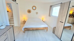 Une chambre à coucher avec un lit en bois, deux lampes de chevet, une petite table ronde, un miroir et un escalier menant à l’étage supérieur.