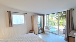 Une chambre comprenant un lit, une chaise, une armoire et une porte-fenêtre coulissante donnant sur un espace extérieur avec une table et des chaises.