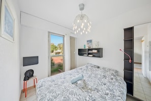 Ein Schlafzimmer mit Bett, Fernseher, Ventilator, Bücherregal und Blick ins Freie.