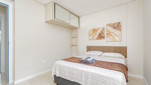 A bedroom with a bed, a built-in shelf, and two marble-patterned wall art pieces. - Apto com 2 Vagas e Churrasqueira Ingleses (Florianópolis)