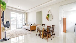 A modern living room with a sofa, dining table, chairs, and a fan. - Apto com 2 Vagas e Churrasqueira Ingleses (Florianópolis)