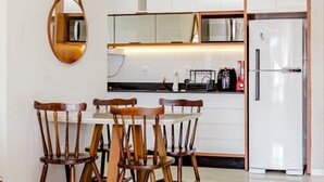 A kitchen with white cabinets, a refrigerator, a microwave, and a coffee machine. There are four wooden chairs around a table. - Apto com 2 Vagas e Churrasqueira Ingleses (Florianópolis)