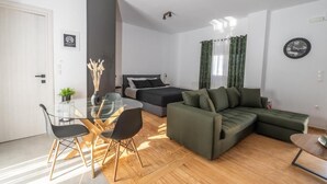 Ein modernes Wohnzimmer mit einem Glastisch, einem grünen Sofa, einem Bett und einer Wanduhr.