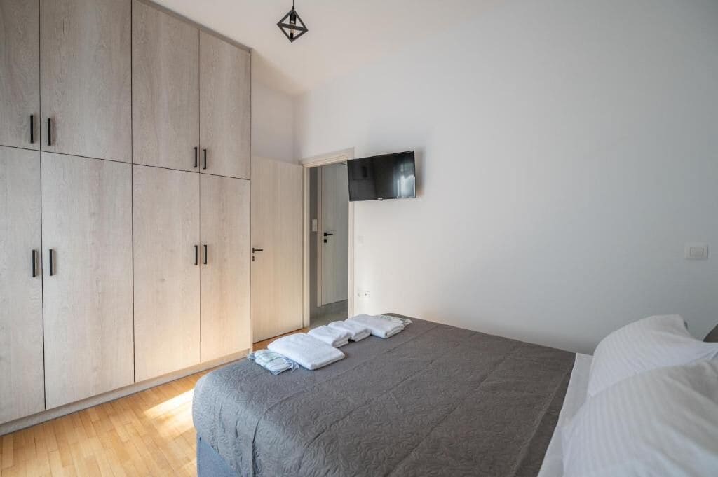 A bedroom with a bed, a wardrobe, and a flat-screen TV mounted on the wall.