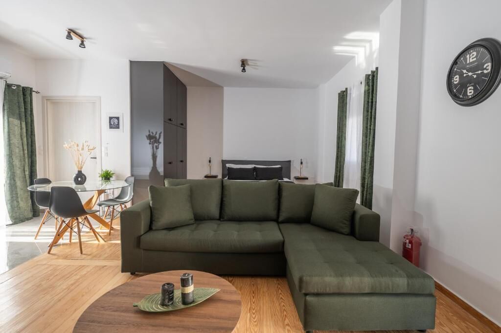 Un salon moderne avec un canapé d’angle, un coin repas doté d’une table en verre et un lit visible au fond de la pièce.