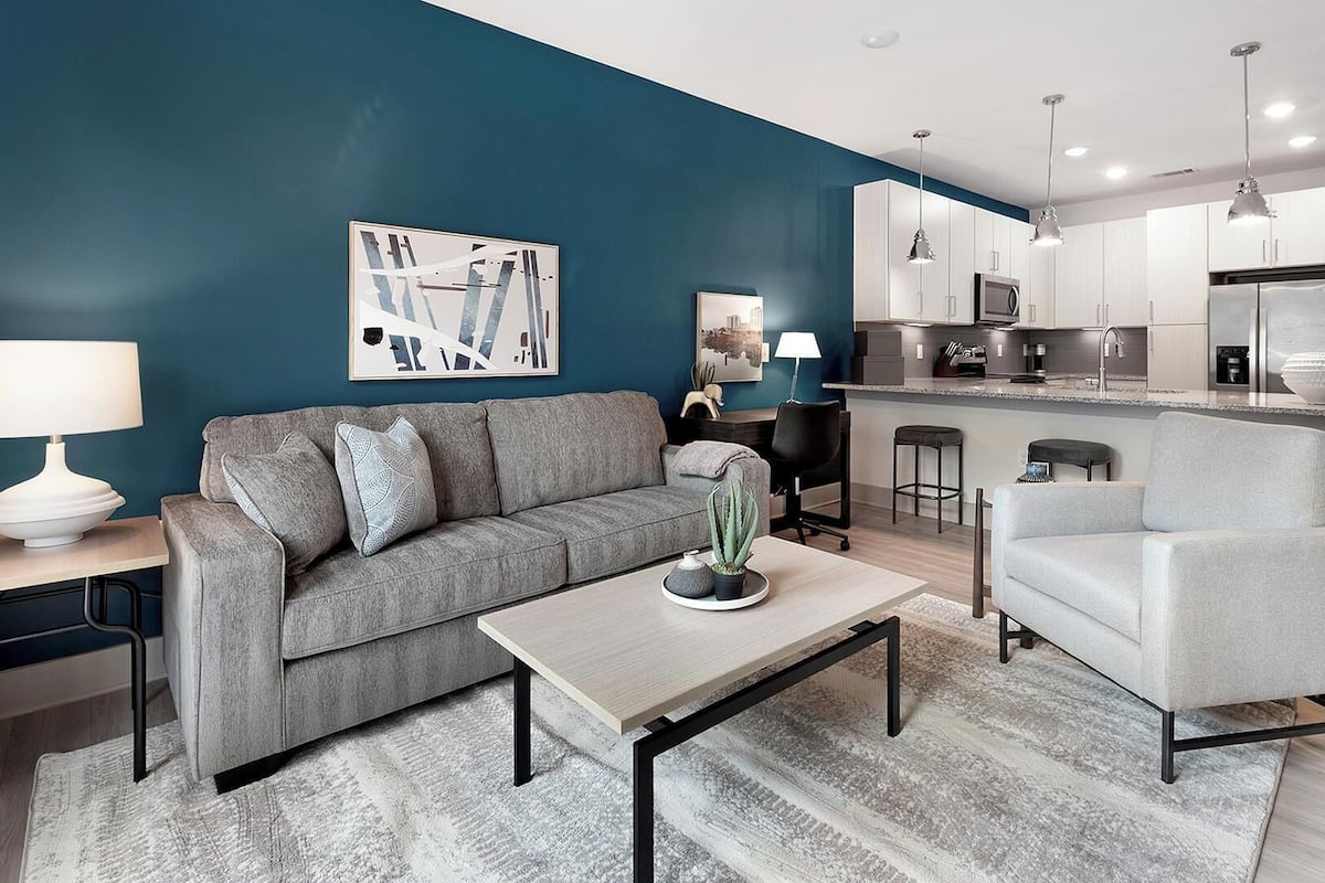 A modern living room with a grey sofa, a coffee table, and a dining area with a bar.