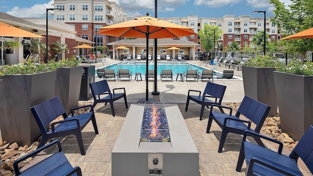 A poolside area with lounge chairs, a fire feature, and umbrellas. - Landing Apartments Near Autumnwood (Charlotte)