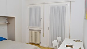 Una camera da letto con un letto, una scrivania con sedie, un termosifone e un armadio con tende.