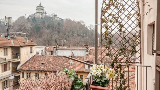 A balcony with a view of a hilltop building, potted plants, and a metal trellis. - Panoramic apartment with a view of the Po River (Torino)