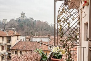 A balcony with a view of a hilltop building, potted plants, and a metal trellis. - Panoramic apartment with a view of the Po River (Torino)