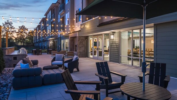 An outdoor patio area with seating arrangements, a barbecue grill, and string lights. - Landing Apartments Near Woodcrest (Raleigh)