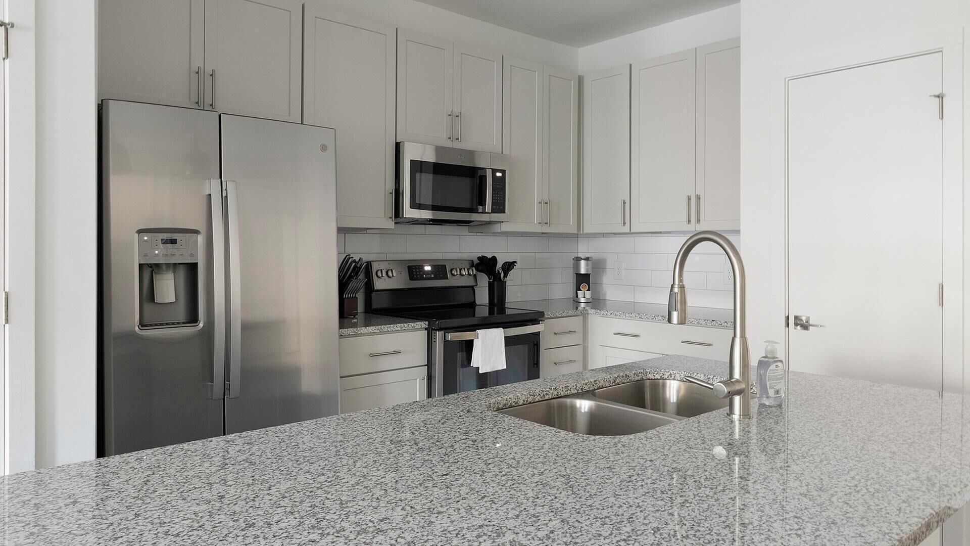 A modern kitchen with stainless steel appliances, granite countertops, and white cabinetry.