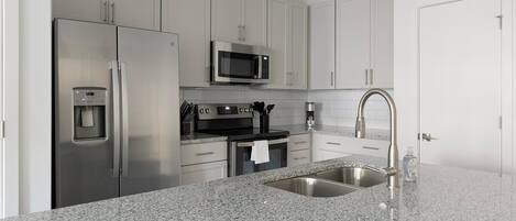 A modern kitchen with stainless steel appliances, granite countertops, and white cabinetry.