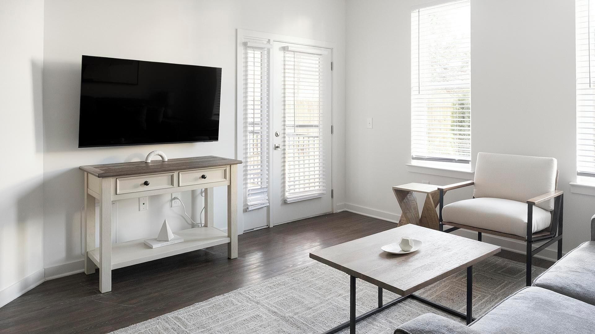 Een moderne woonkamer met een flatscreen-tv, een witte console tafel, een grijze bank en een salontafel.