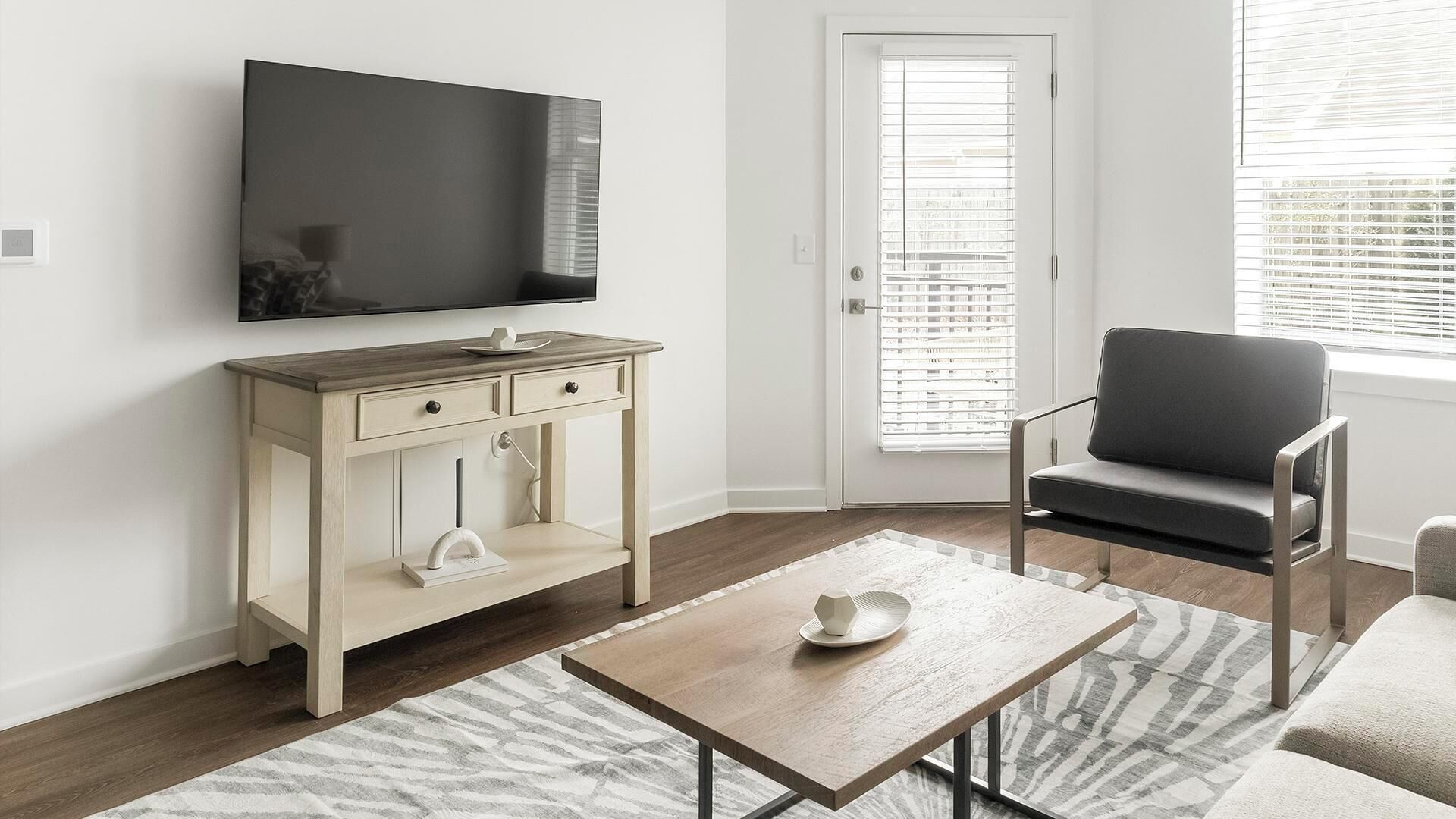 A modern living room with a TV, a wooden cabinet, a grey sofa, and a patterned rug.