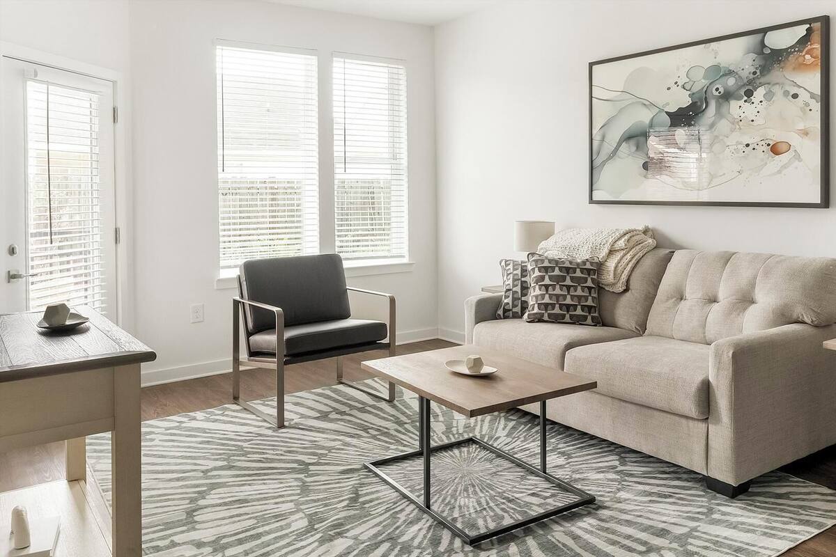 Una sala de estar con sofá, sillón, mesa de centro, mesita auxiliar y una obra de arte en la pared.