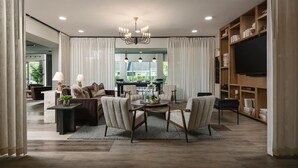 A spacious living room with a dining area, a chandelier, and a television on the wall. - Landing Apartments Near Woodcrest (Raleigh)
