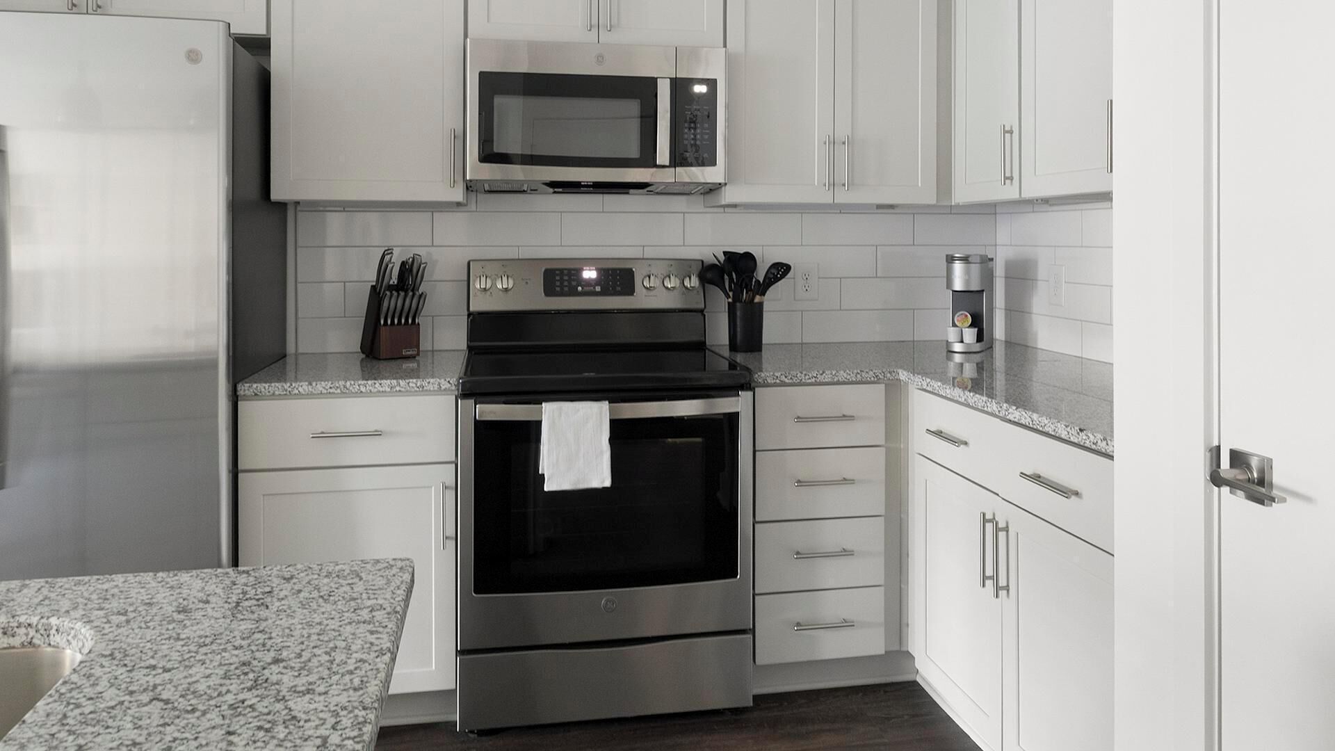 A modern kitchen with white cabinets, a stainless steel refrigerator, a microwave, an oven, and a coffee machine.