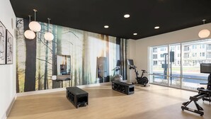 A spacious room with a large window, a wall-mounted TV, exercise equipment, and a sound system. - Landing Apartments Near Woodcrest (Raleigh)